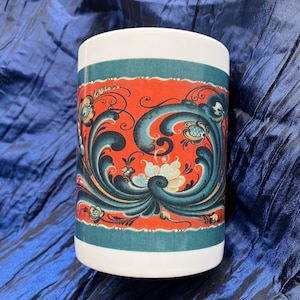 May include: A white ceramic cylinder vase with a vibrant, ornate design. The design features a red background with teal and dark blue floral patterns. The top and bottom of the vase are white, creating a striking contrast.