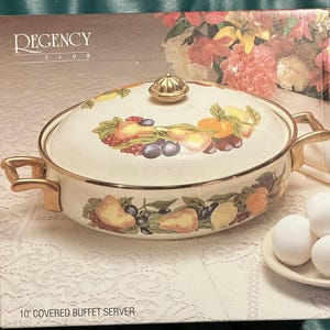 May include: A 10-inch covered buffet server with a white base and gold trim. The lid features a colorful fruit design with pears, oranges, and berries. The server is part of the Regency Club collection.