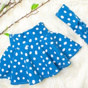 Könnte beinhalten: Ein blauer Rock mit weißen Punkten und einem passenden Stirnband. Der Rock ist aus weichem, dehnbarem Stoff und hat einen gerafften Bund. Das Stirnband ist ein einfaches, dehnbares Band mit einer Schleife oben.