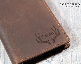 May include: A brown leather wallet with a personalised inscription of "Smith" and an engraved antler design. The wallet is stitched with brown thread and has a distressed leather look.