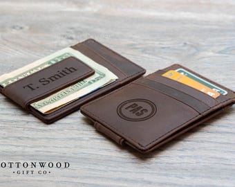 May include: Two brown leather wallets with money clips. One wallet has the name "T. Smith" engraved on it. The other wallet has the initials "PAS" engraved on it.