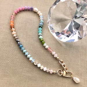 Pode incluir: Um colar de contas de arco-&iacute;ris com um fecho dourado e um fecho de p&eacute;rola. O colar &eacute; feito com v&aacute;rias pedras semipreciosas.