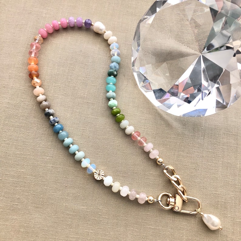 Pode incluir: Um colar de contas de arco-&iacute;ris com um fecho dourado e um fecho de p&eacute;rola. O colar &eacute; feito com v&aacute;rias pedras semipreciosas.