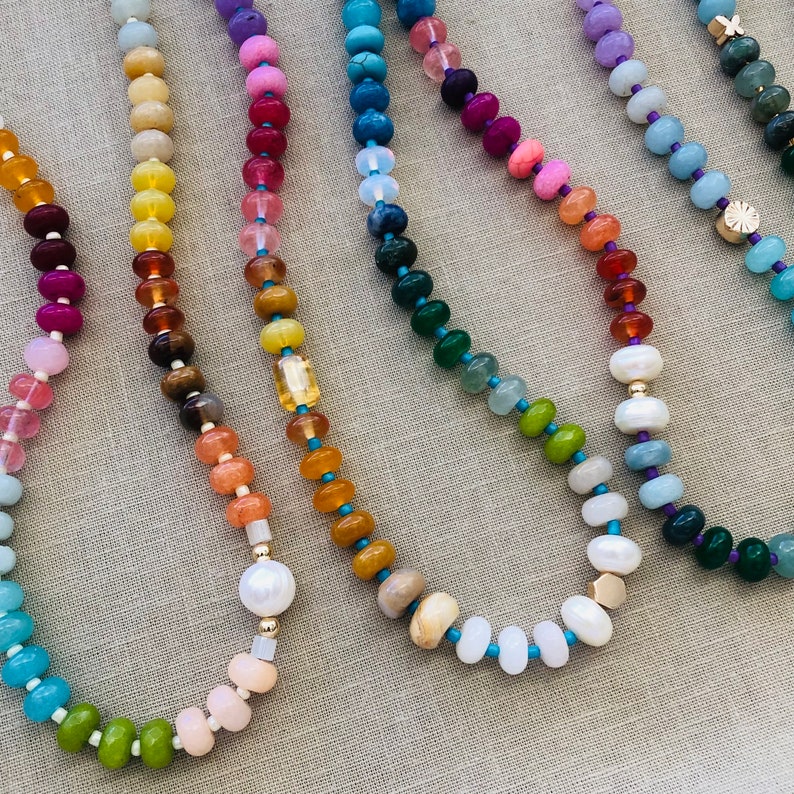 Pode incluir: Uma cole&ccedil;&atilde;o de colares de contas coloridas com diferentes contas de pedras preciosas, incluindo turquesa, ametista e jade. Os colares est&atilde;o dispostos em um padr&atilde;o de arco-&iacute;ris.