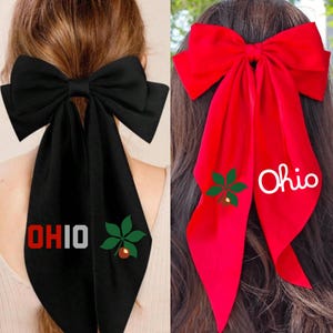 May include: Two hair bows with long tails, one black and one red. Both bows have a green buckeye leaf and the word "Ohio" embroidered on them.