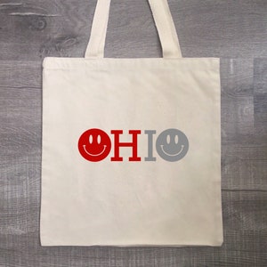May include: A white canvas tote bag with red and gray smiley faces and the word "OHIO" printed on it.