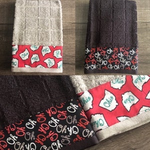 May include: Two kitchen towels with red and white patterned borders. One towel is gray and the other is black. The border features the state of Ohio and the words "Ohio" and "Oh yo".