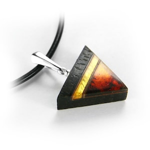 May include: A triangular pendant necklace with a black wood base and a red and gold resin inlay. The pendant is attached to a black leather cord.