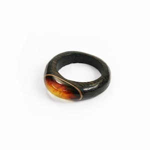 Puede incluir: Un anillo de madera oscura con una piedra de ámbar transparente engastada en la banda.