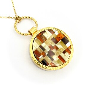 May include: A gold necklace with a round pendant featuring a mosaic of amber stones in various shades of brown, white, and black.