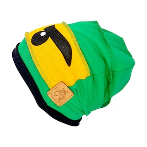 Könnte beinhalten: Grün-gelbe Mütze mit einem schwarz-weißen Vogelmotiv. Die Mütze hat einen schwarzen Saum und ein braunes Lederlabel mit dem Text "Schnuckelgrunes" und einem Marienkäfer-Motiv.