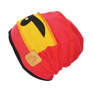 Könnte beinhalten: Rote und gelbe Strickmütze mit einem schwarzen Augenklappen-Design und einem braunen Leder-Etikett mit der Aufschrift "Somewhere over the rainbow".