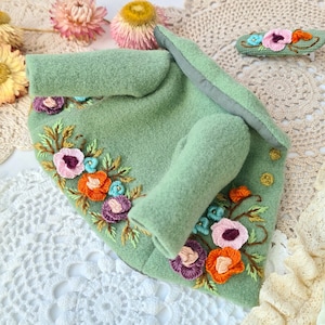 Può includere: Una giacca di feltro verde con fiori ricamati in tonalità di rosa, arancio e viola. La giacca ha un colletto e una manica lunga.