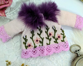 May include: A pink corduroy jacket with a purple fur collar and pink lace trim. The jacket is embroidered with green vines and pink flowers.