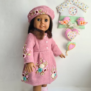 May include: A pink doll wearing a pink coat with floral embroidery, a pink beret, and pink socks. The doll has brown hair and brown eyes. The doll is standing in front of a white background with a pink birdhouse hanging above.