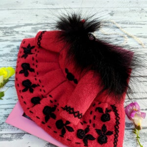 May include: A red felt doll dress with black embroidery and a black faux fur trim.