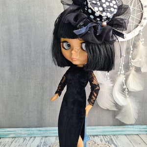 May include: A black and white polka dot top hat with a black tulle bow and a black velvet dress with lace sleeves. The doll has black hair and blue eyes.