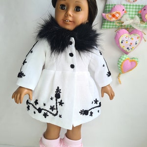 May include: A white doll wearing a white coat with a black faux fur collar and black embroidery. The doll has brown skin and black hair. The doll is wearing pink socks.