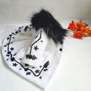 May include: A white embroidered jacket with black floral designs and a black fur collar.