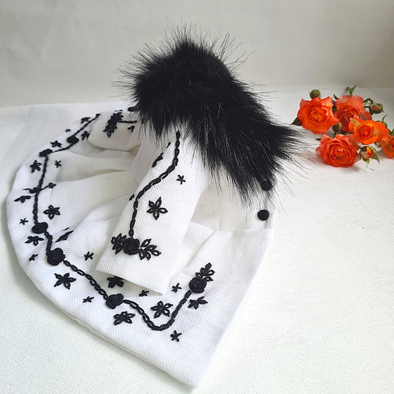 May include: A white embroidered jacket with black floral designs and a black fur collar.