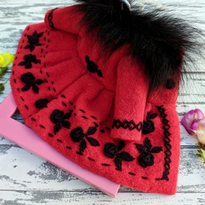 May include: A red felt doll dress with black embroidery and a black faux fur collar.
