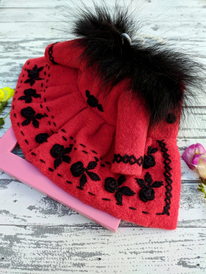 May include: A red felt doll dress with black embroidery and a black faux fur collar.