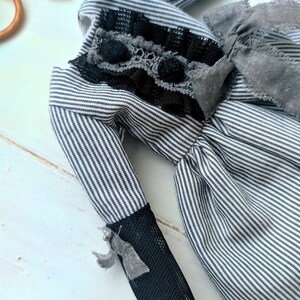 May include: A handmade doll with a black and white striped fabric body. The doll has black lace and grey fabric accents on the bodice and sleeves. The sleeves are finished with black mesh and small grey bows.