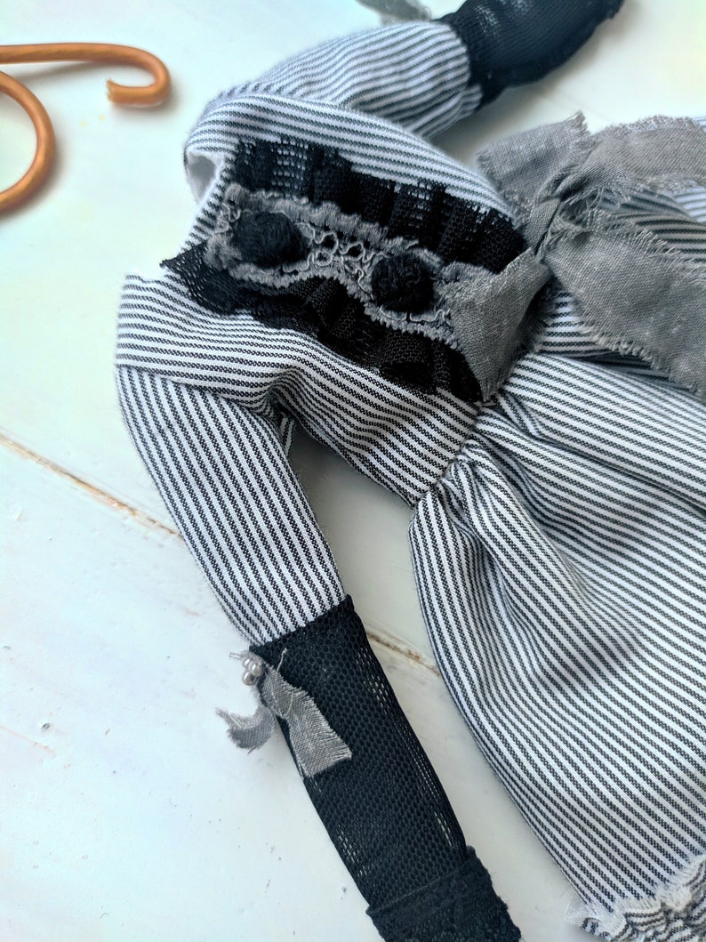 May include: A handmade doll with a black and white striped fabric body. The doll has black lace and grey fabric accents on the bodice and sleeves. The sleeves are finished with black mesh and small grey bows.