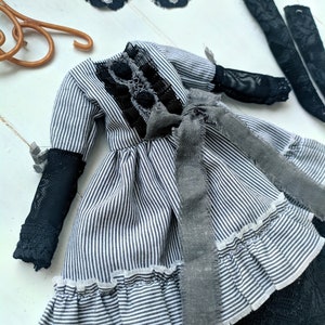 May include: A miniature dress with black and white stripes, featuring black lace details and a grey ribbon. The dress has long sleeves with black mesh cuffs and a ruffled hem. Additional black lace and accessories are also visible.