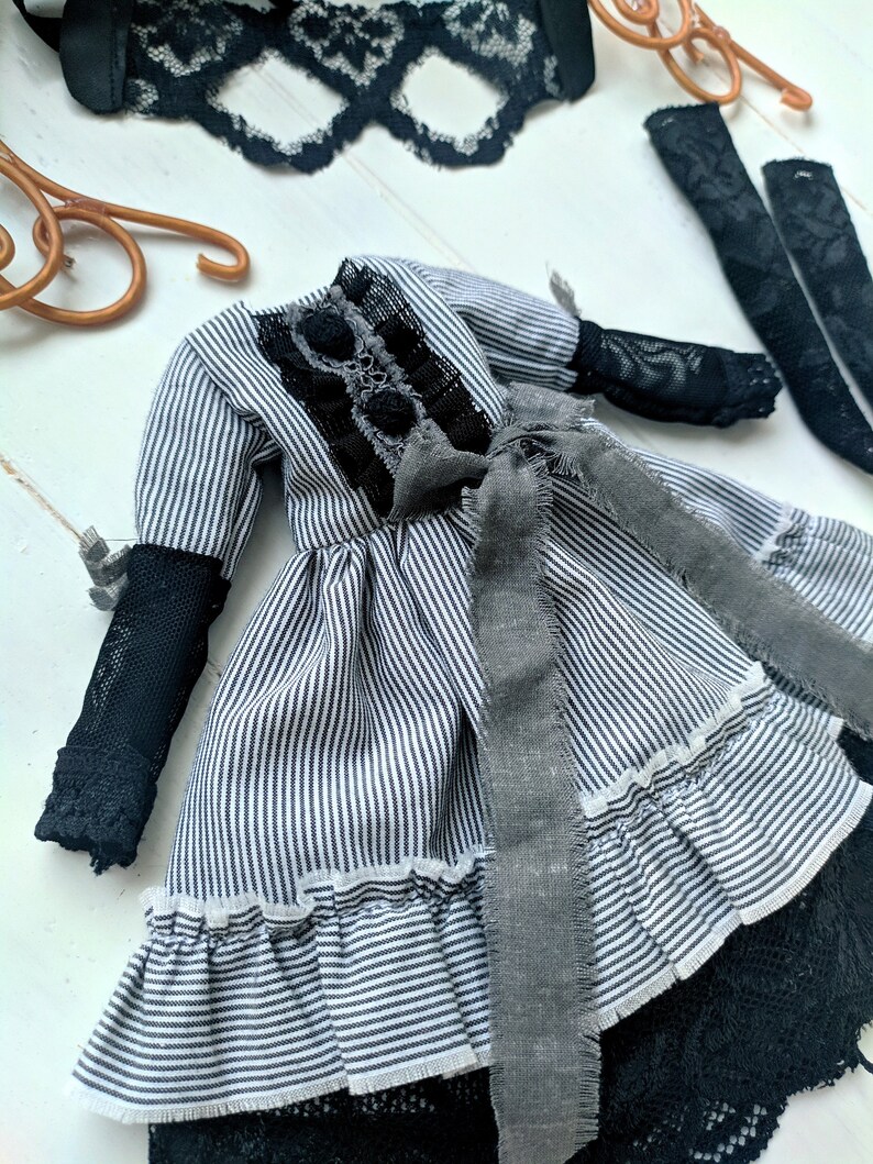 May include: A miniature dress with black and white stripes, featuring black lace details and a grey ribbon. The dress has long sleeves with black mesh cuffs and a ruffled hem. Additional black lace and accessories are also visible.