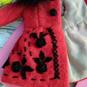 May include: A red wool coat with black fur trim and black embroidered flowers. The coat has a white lining and black buttons.