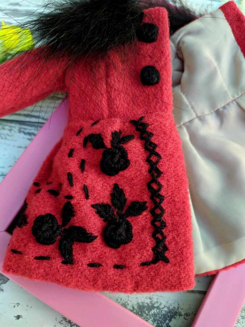 May include: A red wool coat with black fur trim and black embroidered flowers. The coat has a white lining and black buttons.