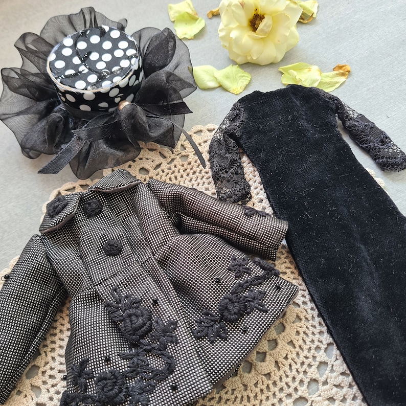 May include: A black and white polka dot hat with a black lace trim, a black dress with lace sleeves, and a black and white patterned jacket with black lace trim.