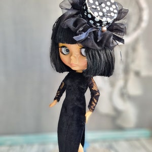 May include: A black and white polka dot top hat with black tulle and a black velvet dress on a doll with black hair and large eyes.