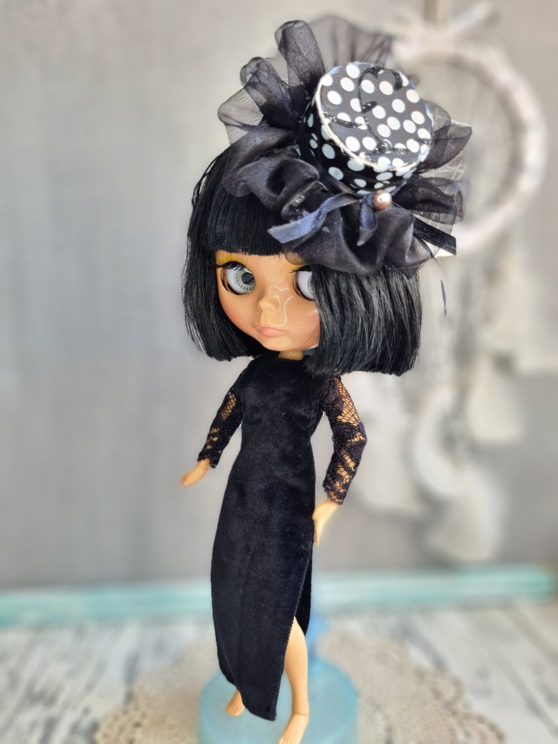 May include: A black and white polka dot top hat with black tulle and a black velvet dress on a doll with black hair and large eyes.