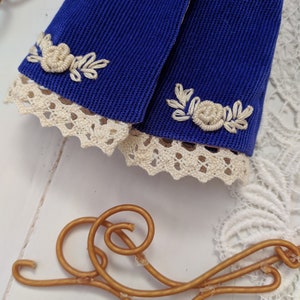 May include: Two blue fabric sleeves with white lace trim and white embroidered floral designs.
