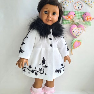 May include: A doll wearing a white coat with black embroidery and a black fur collar. The doll has brown skin, brown eyes, and black hair. The doll is wearing pink socks.