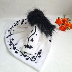 May include: A white embroidered jacket with black floral designs and a black faux fur collar.