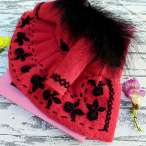 May include: A red felt doll dress with black embroidery and a black fur trim around the neckline.