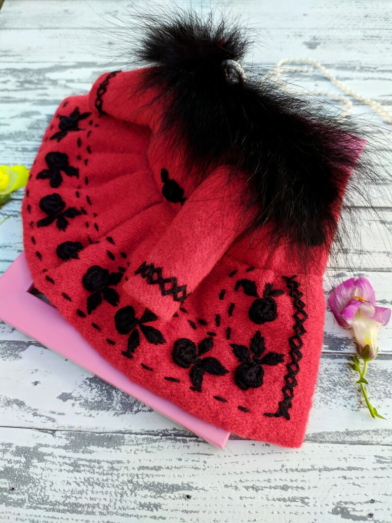 May include: A red felt doll dress with black embroidery and a black fur trim around the neckline.