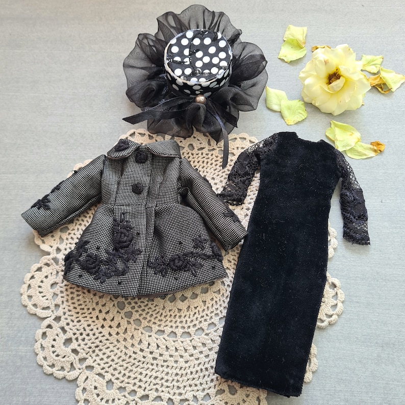 May include: A black and white polka dot hat with a black lace trim, a black velvet dress with lace trim, and a black and white patterned jacket with lace trim.
