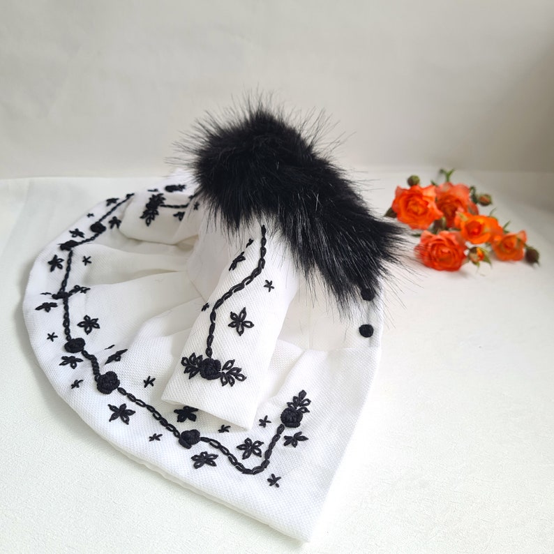 May include: A white faux fur jacket with black embroidery and a black fur trim around the collar.