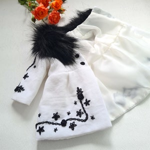 May include: A white baby coat with a black faux fur collar and black embroidered floral details.