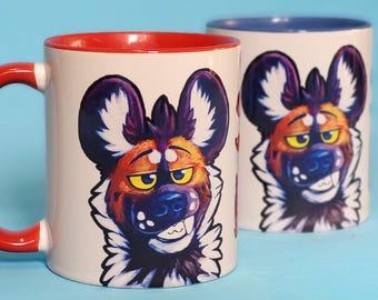 May include: Two white ceramic mugs with red and blue rims. The mugs feature a colorful illustration of a cartoon African wild dog with a white, black, and orange fur pattern. The text "motomo WahoTs" is printed above the mugs.