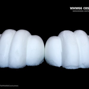 May include: Two white foam hands, each with three fingers, are shown against a black background. The hands are curved and appear to be part of a costume.