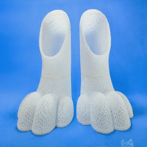 May include: Two white, textured, 3D-printed feet, each with a long, open tube and three toes. The feet are set against a bright blue background. The text "WMW66 COSTUMES" and a website address are visible at the bottom.