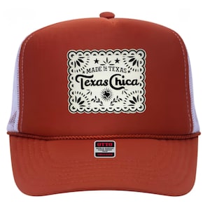 May include: A burnt orange trucker hat with a white mesh back. The front features a decorative patch with the words "MADE IN TEXAS" and "Texas Chica" in a black, ornate font. The hat also has a small "OTTO" label.