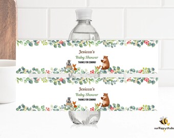 May include: Water bottle label with a woodland theme. The label features a green leafy border with red berries and a white background. The text on the label reads "Jesicca's Baby Shower Thanks for coming!" and features a cartoon bear, fox, and raccoon.