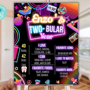 May include: A neon pink and blue birthday poster with the text "Enzo's Two-Bular Year" and a list of facts about the birthday person, including their age, weight, height, favorite foods, and favorite activities. The poster is decorated with 80s-themed graphics, such as roller skates, cassette tapes, and a Rubik's cube.
