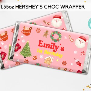 May include: Pink and silver Hershey's chocolate bar wrapper with a Christmas theme. The wrapper features a gingerbread house, a Christmas tree, Santa Claus, candy canes, and the text "Emily's 1st Birthday".